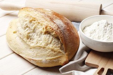 loaf of homemade bread with kitchen accessories and baking ingredients on a wooden table with place for text. Fresh bakery.