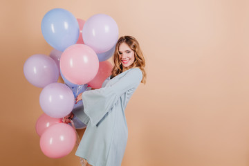 Adorable blonde white woman in blue attire posing with beautiful balloons. Indoor photo of cute birthday girl enjoying celebration.