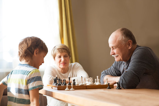 Grand Parent With Grandson Play Chess Together At Home. Quarantine. Health Concept. Corona Virus.  Quality Time. Family Having Fun Playing At Home. Stay Home Concept