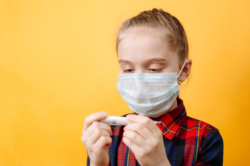 A Teenage girl In a medical Mask Looks at a Thermometer