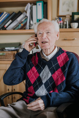 Elderly man talking on phone sitting at home