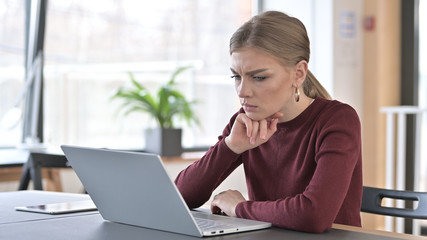Pensive Young Woman Reading on Laptop in Office