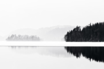 Fototapeta premium Trees reflected in water a misty winter day, Sweden.