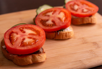 Slices of tomatoes and cucumbers on slices of wheat bread on a cutting Board close-up.
