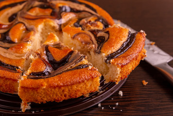 Cut into pieces round cake with chocolate and caramel on the table. The knife is lying nearby.