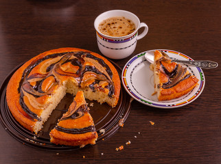 Cut into pieces round cake with chocolate and caramel on the table. A Cup of coffee is next to it.
