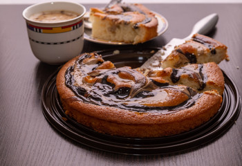 Cut into pieces round cake with chocolate and caramel on the table. The knife is lying nearby.