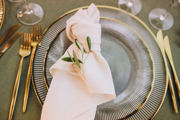 Banquet table served with glass plates with napkins, gold cutlery and glasses