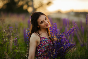 Young beautiful girl holding a large flower with purple lupine in a flowering field. Blooming lupine flowers.
