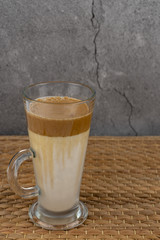 Iced Dalgona Coffee, a trendy fluffy creamy whipped coffee in a tall glass over wooden background.