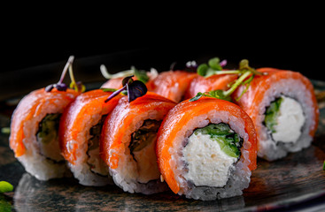 sushi roll with salmon, avocado, cream cheese in plate on black wooden table background