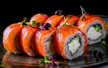 sushi roll with salmon, avocado, cream cheese in plate on black wooden table background