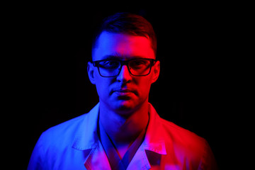 Portrait of a doctor or medical specialist. Horizontal portrait. Man in scrubs. Black background with blue and red light. Closeup.