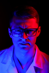 Fototapeta na wymiar Studio portrait of a doctor or medical specialist. Standing in glasses. Man in scrubs. Black background with blue and red light. Closeup.