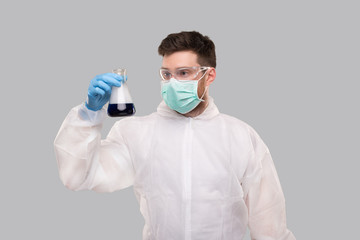 Male Laboratory Worker in Chemical Suit, Wearing Medical Mask and Glasses Watching Flask with Colorfull Liquid. Science, Medical, Virus Concept