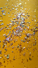 Foil pieces on yellow background with multi-colored shine. Abstract fashion stock macro photo.