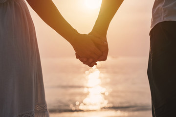 Young woman traveler holding man's hand and looking beautiful sunset on the beach, Couple on vacation in summer concept
