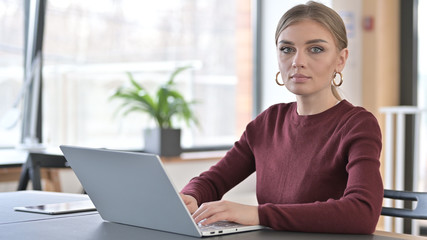 Young Woman with Laptop Looking at Camera in Office
