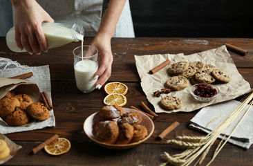 Woman pours cow's milk into a glass on a wooden table with homemade cookies