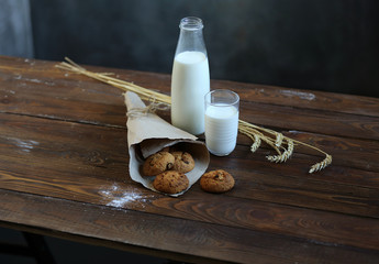 On a wooden table, a bottle and a glass of milk, homemade cookies packed in craft paper