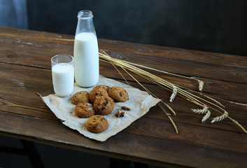 Bottle of milk, glass of milk, wheat spikelets, cookies for breakfast on a brown wooden table