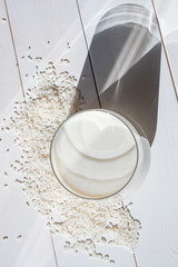 Rice milk in a transparent glass on a light wooden background. Rice is scattered nearby. Bright...