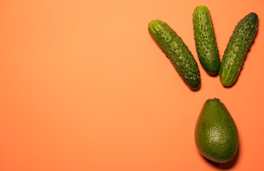 The vegan concept of healthy food - cucumbers and avocado on a peach background. The concept of an idea and a light bulb