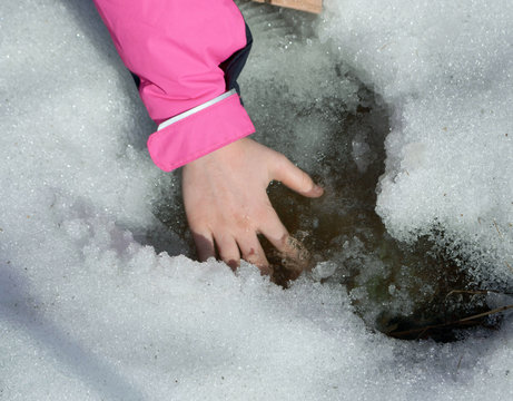 
man’s hand lies in frozen water and snow