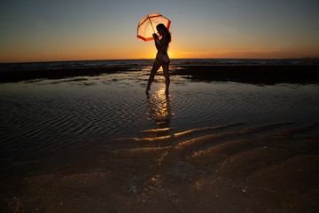 Obraz premium Silhoutte of a pretty senior Asian female in a swimming suit standing and hold umbrella posing on the beach..