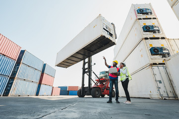Two Black foreman worker working at Container cargo harbor holding laptop computer and using walkie-talkie to loading containers. African dock male and female  Logistics import export concept.