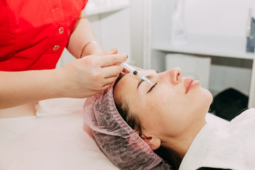 Obraz na płótnie Canvas Close up of hands of expert beautician injecting botox in female forehead. The woman closed her eyes with joy. She is gently smiling