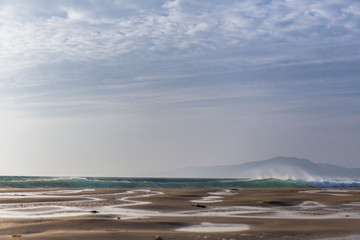 beach with a large strip of sand, in the background you can see some waves and the silhouette of the African continent, cloudy day