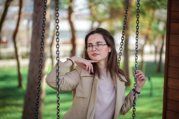 Portrait of a stylish girl in glasses, closeup. Leisure. Beautiful woman looking at the camera while sitting on a swing.