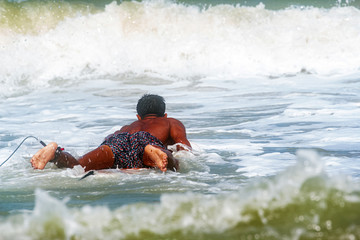 Back side of young man laying down on longboard,surfing,water sport,splash of sea water around
