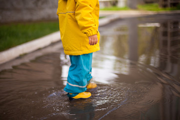 little feet of a child in rubber boots and a waterproof suit walk on the water.