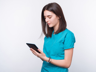 Photo of a smiling girl is wearing medical uniform is looking in his phone on white background.