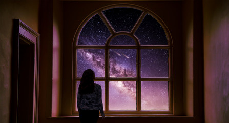 The girl at the window at night dreaming and admiring the milky way sky.