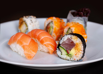 Sushi menu with salmon, rice and tuna rolls on a plate with black background. Japanese food. Close up with selective focus.