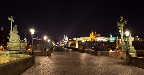 Fototapeta premium Baroque statue of Jesus Christ on the Prague Charles Bridge with the gothic Castle in the Night without People at the time of Coronavirus, Czech republic