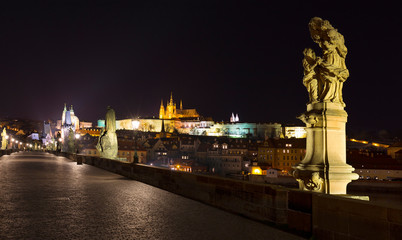 Night colorful Prague gothic Castle with St. Nicholas' Cathedral and Bridge Tower from Charles Bridge with its baroque Statues without People at the time of Coronavirus, Czech Republic