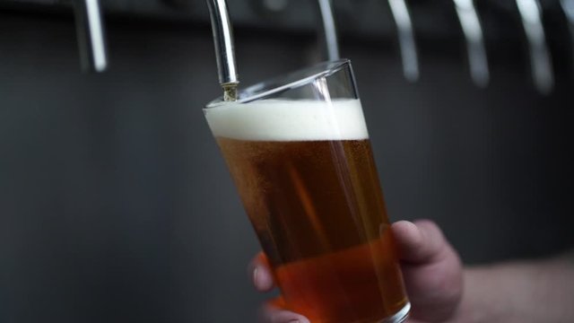 close up shot of bartender's hands pouring a pint of beer from stainless steel tap