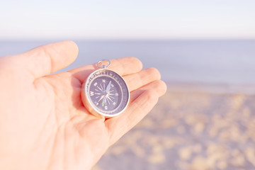 Male hand with magnetic compass on sea shore.