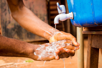 young black person washing her hands with soap under a tap of water