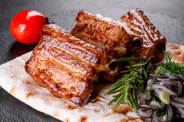 Fried ribs with rosemary, onion, sauce on a concrete background. Dark table. Place for text, copy space