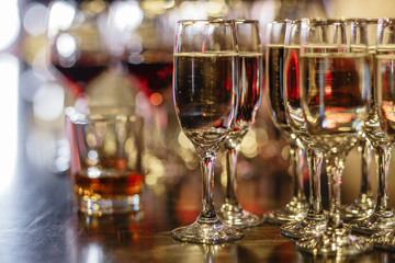 Several glasses of bubbly champagne stands close up against a background of blurry glass of whiskey and wineglasses. The concept of a party table and expensive alcohol. Place for advertising