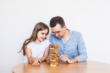 Girl and dad play a game at home, cost a tower of blocks, cubes, jenga, puzzle for brain development, mental intelligence, child development, school, home, quarantine, vacation, time with family