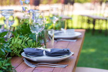 Beautifully decorated wooden table in a summer open-air cafe. Green branch and fresh flowers table decoration