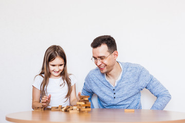 Girl and dad play a game at home, cost a tower of blocks, cubes, jenga, puzzle for brain development, mental intelligence, child development, school, home, quarantine, vacation, time with family