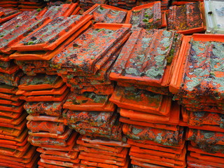 Tejas de barro con musgo y liquen amontonadas en el campo.