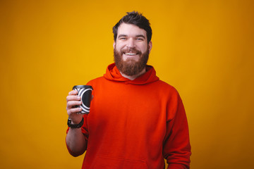 Photo of bearded man on yellow background is holding a black and white coffee paper to go cup.